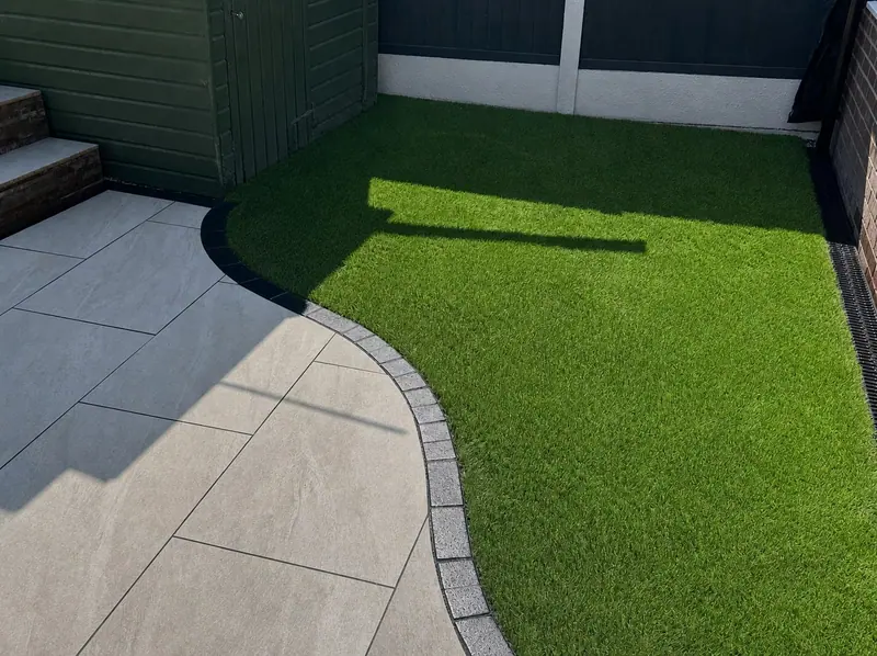 Artificial lawn with curved block edging and grey porcelain paving