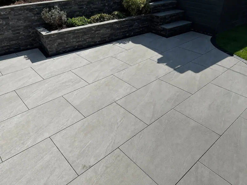 Grey paved patio with raised stone planters and steps