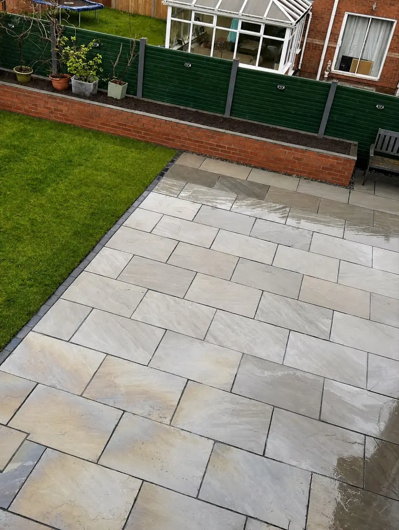 Grey paving beside an artificial lawn and raised brick planting bed