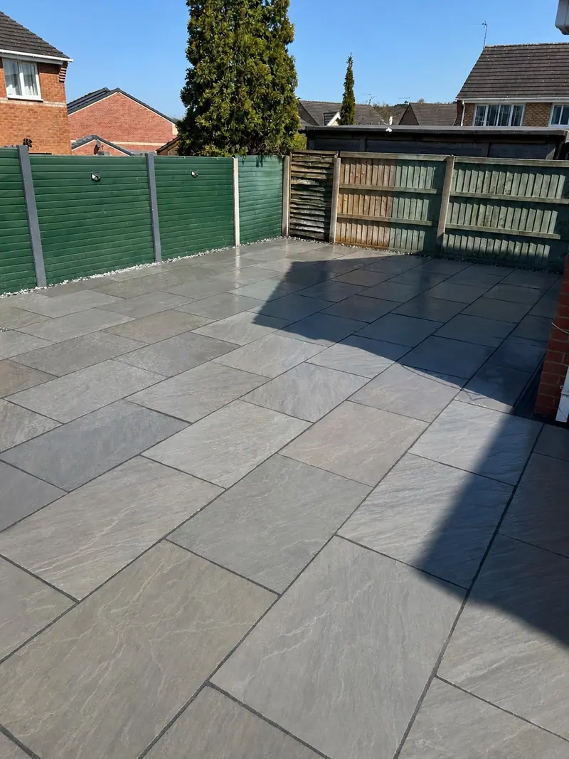 Large grey paved patio beside garden screening