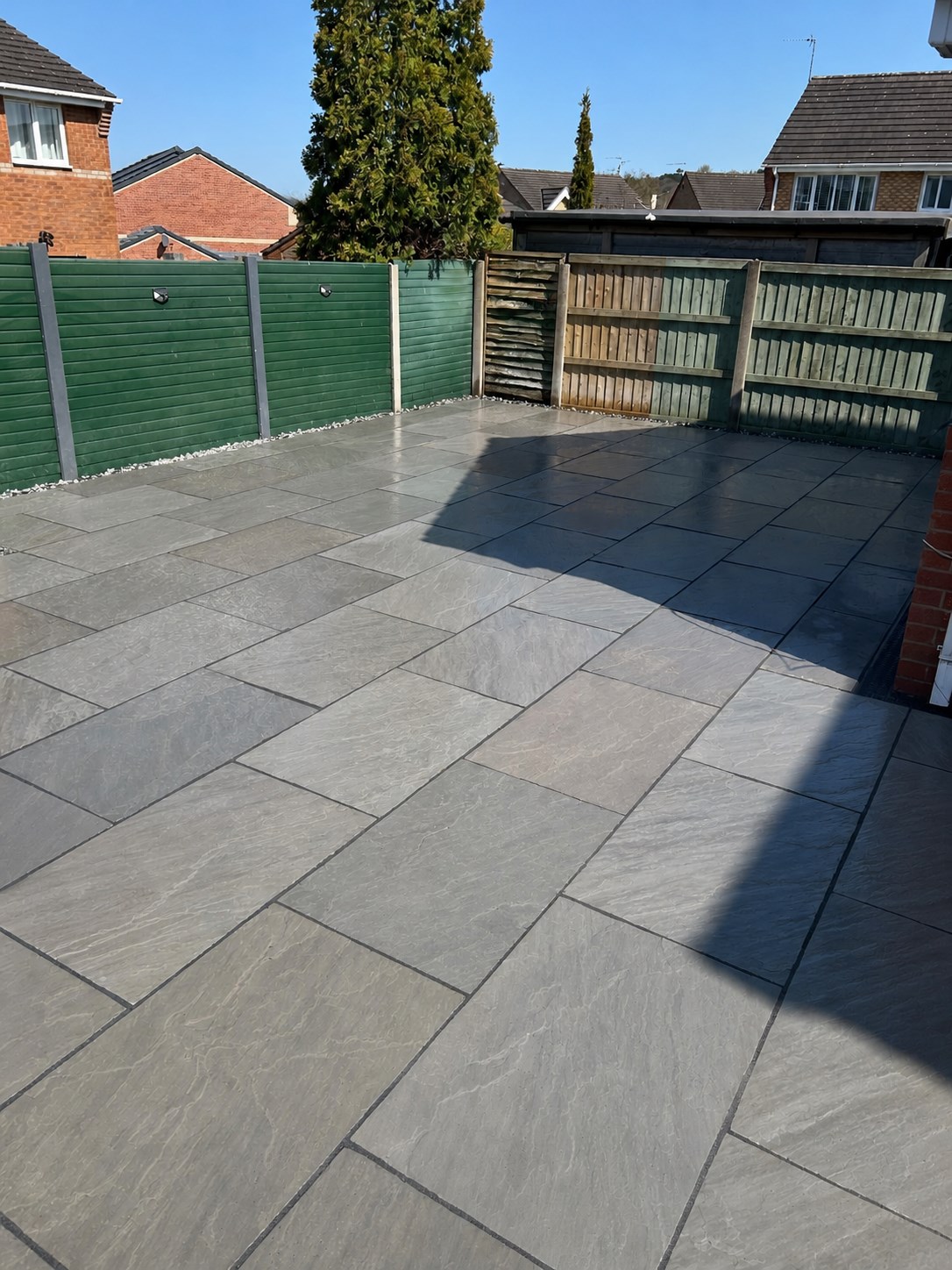 Large grey paved patio beside garden fencing